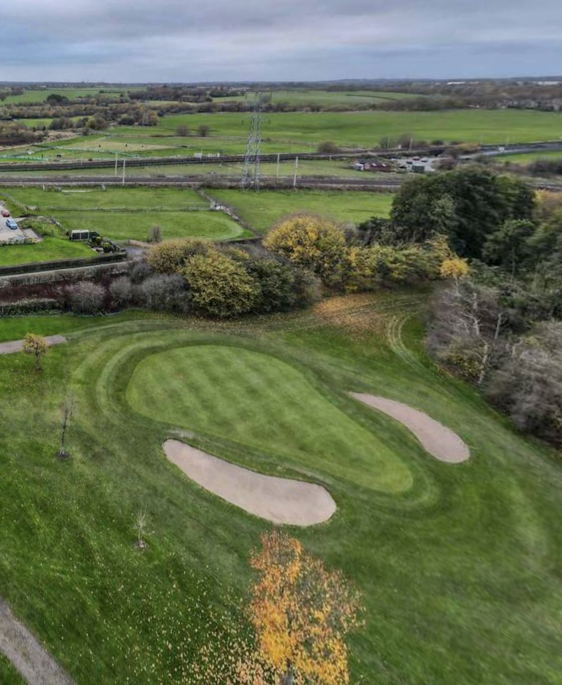 Aerial view of a verdant golf course green flanked by bunkers, with open countryside beyond